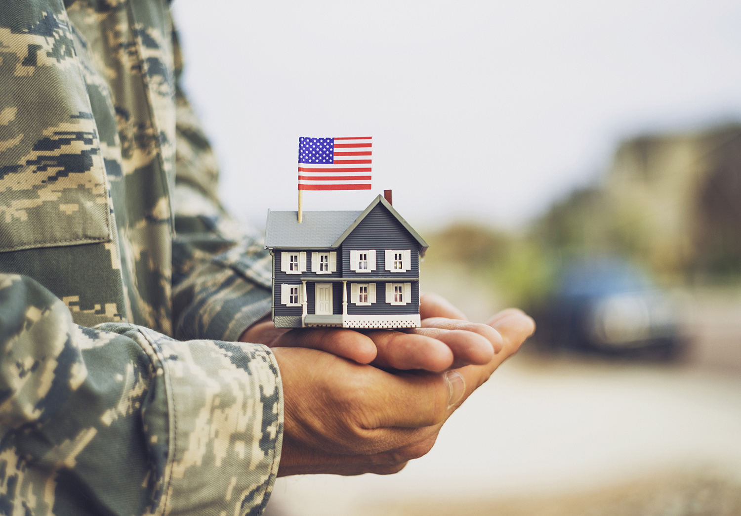 Military Person Holding a model home with a flag